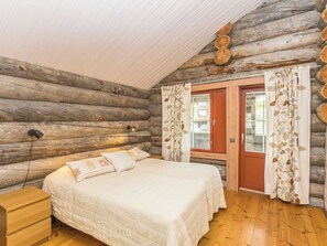 Une chambre dans un chalet en rondins, avec un lit, une commode en bois et une fenêtre avec des rideaux.