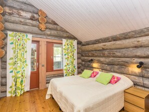 Ein Schlafzimmer in einer Blockhütte mit einem Bett, Vorhängen und einem Nachttisch.