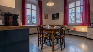 Un comedor con mesa y sillas de madera, una cafetera y cortinas rojas.