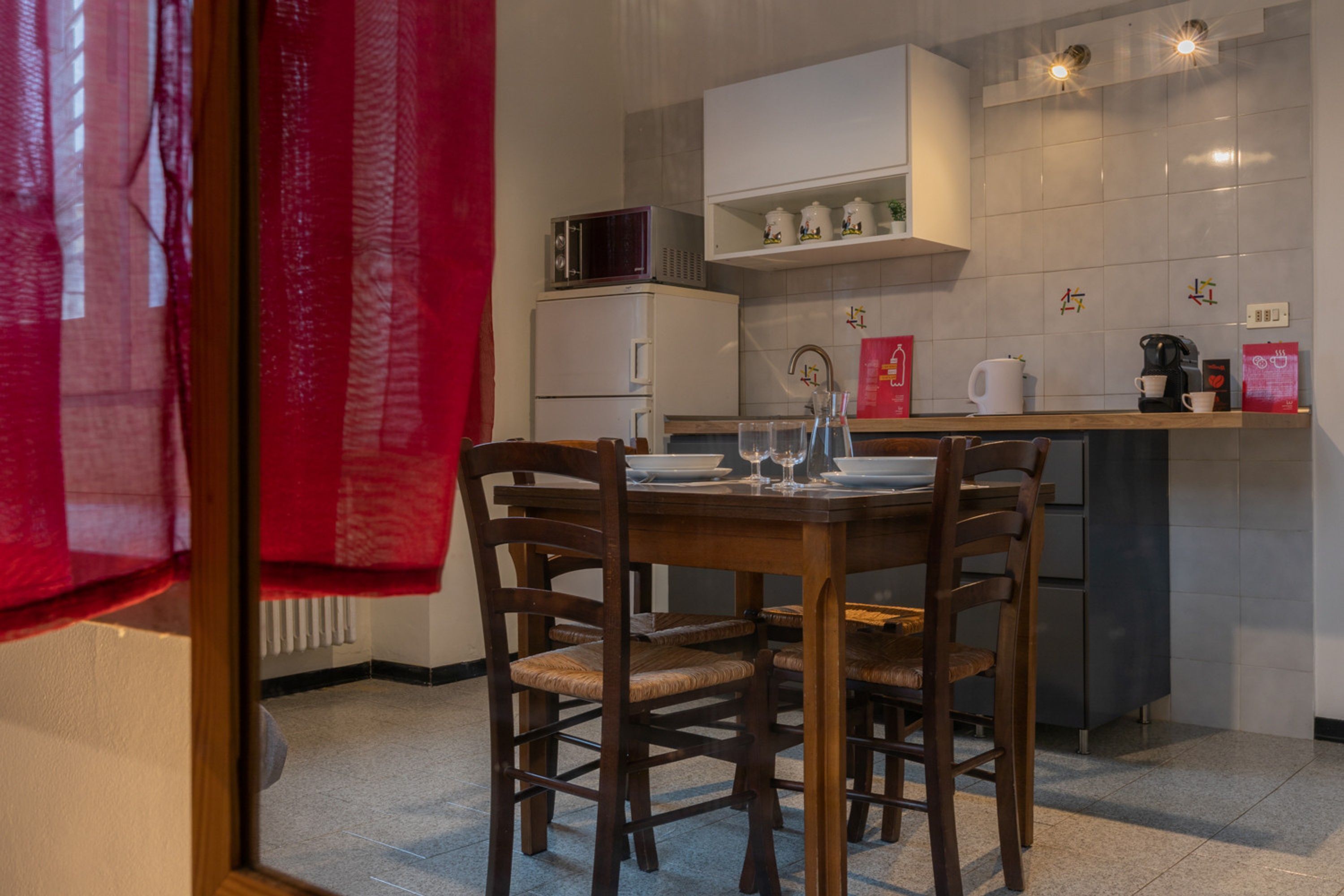 A dining area with a wooden table and chairs, a microwave, and a small kitchen counter with a kettle and coffee maker.