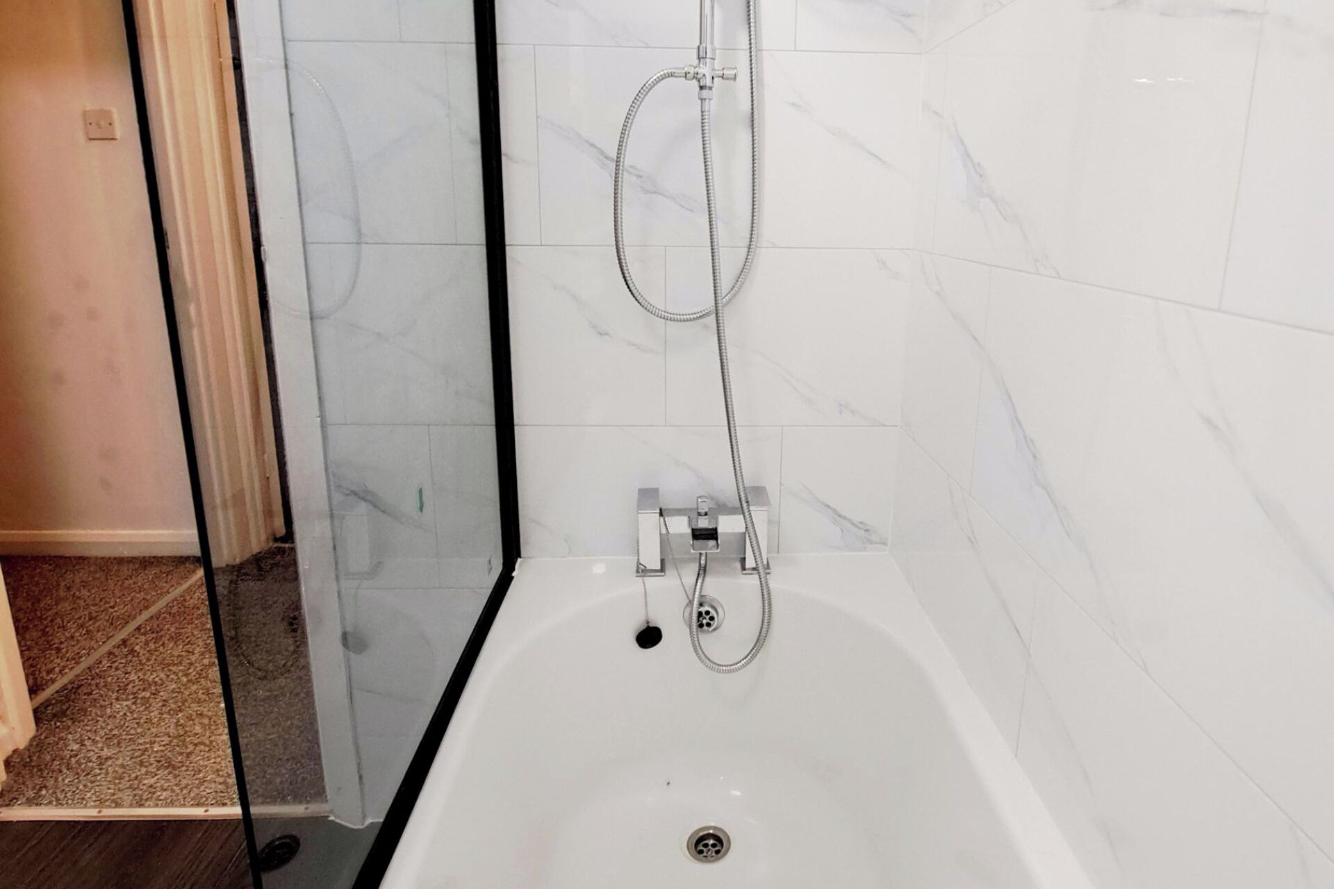 A bathroom with a bathtub, a shower with a handheld hose, and a glass shower enclosure.
