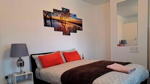 A bedroom with a bed, a nightstand, a lamp, a mirror, and a wall art piece. - 2 Bedroom House in Leeds - Sleeps 5, Wifi, Pets (Leeds)