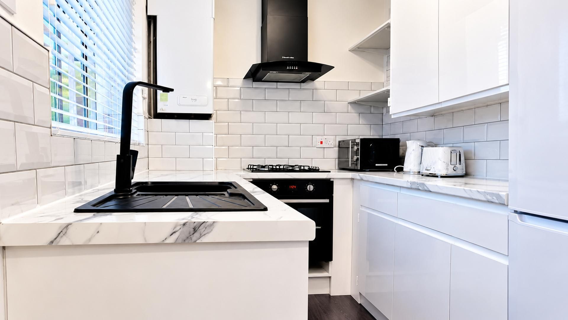 A modern kitchen with white cabinetry, a black range hood, and a built-in oven.