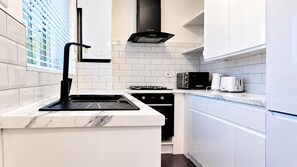 Une cuisine moderne avec des meubles blancs, une hotte noire et un four encastré.