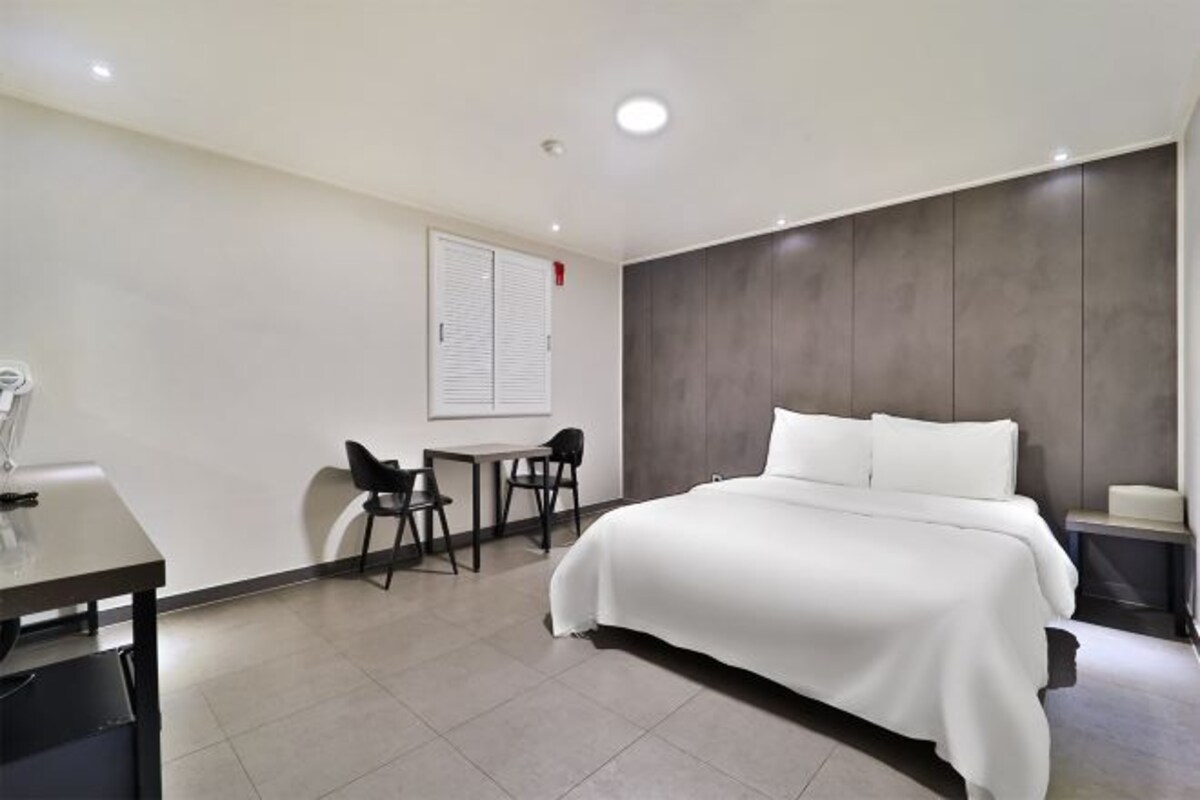 A modern hotel room with a large bed, a desk, two chairs, and a small table.