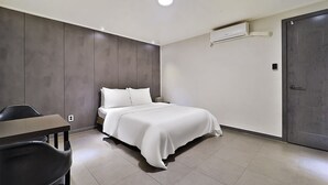 A modern hotel room with a bed, a desk, and a chair. There is an air conditioning unit on the wall and a door to the right. - Anyang Livera (Anyang)