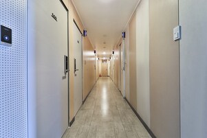 Corredor de hotel com portas com as indicações 500 e 510, um extintor de incêndio e um painel de segurança na parede esquerda.