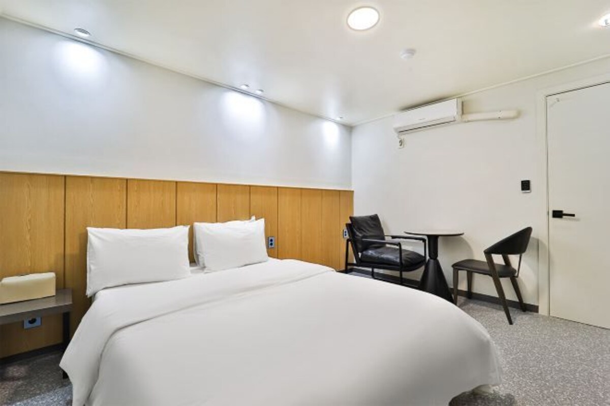A hotel room with a bed, a small table, two chairs, and a door.