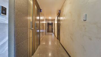 A modern hotel hallway with elevators and a fire alarm on the wall.