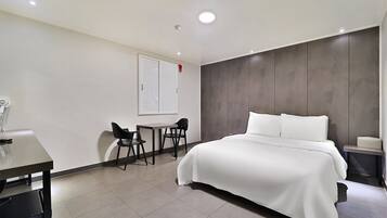 A modern hotel room with a large bed, a desk, two chairs, and a small table.