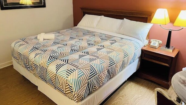 Habitación de hotel con cama, dos lámparas de noche, mesita de noche y un cuadro en la pared.