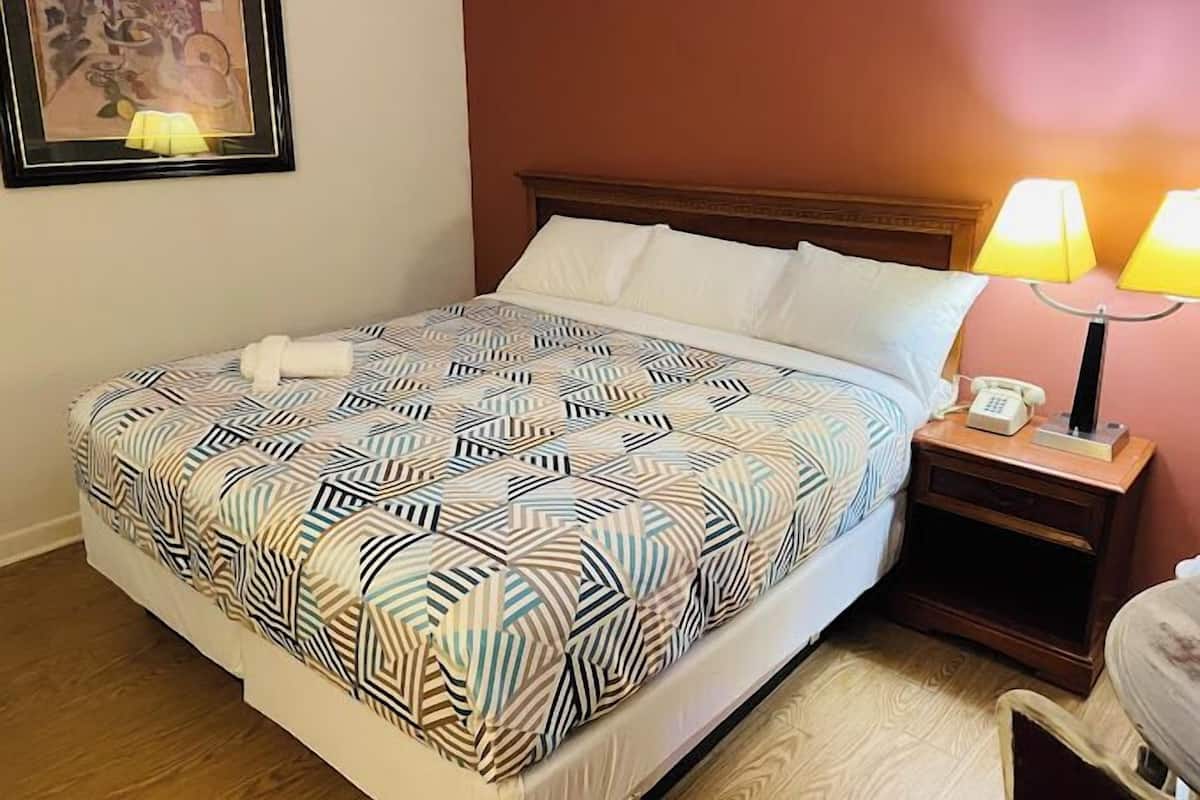 A hotel room with a bed, two bedside lamps, a nightstand, and a framed picture on the wall.