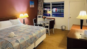 Habitación de hotel con cama, dos lámparas de noche, escritorio con silla, ventana con cortinas y puerta.