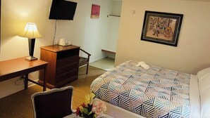 Habitación de hotel con cama, escritorio, silla, televisor y un cuadro en la pared.