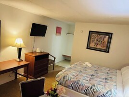Habitación de hotel con cama, escritorio, silla, televisor y un cuadro en la pared.
