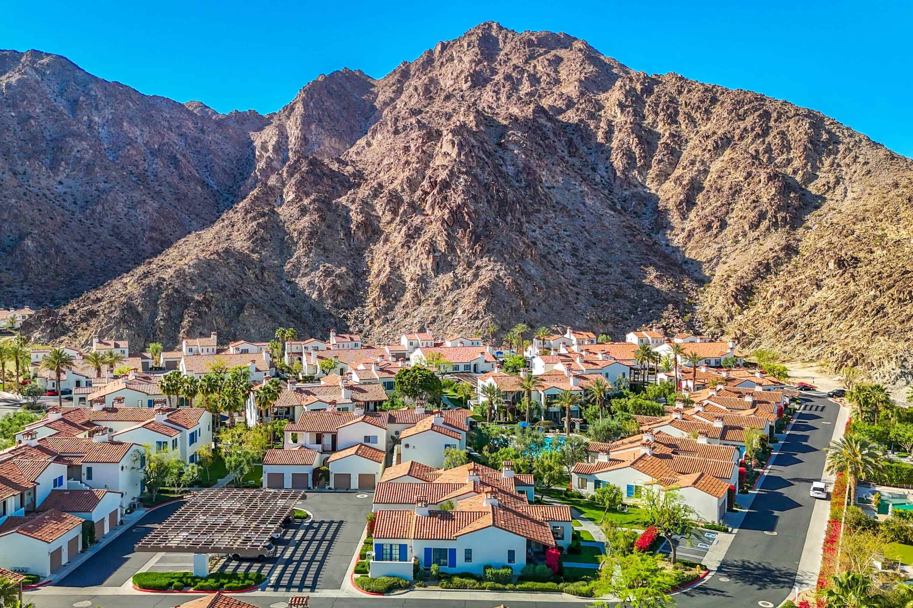A residential area with houses featuring red-tiled roofs, surrounded by mountains.