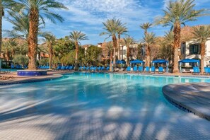 A pool area with blue lounge chairs and palm trees.