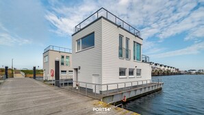 A modern waterfront building with a flat roof, large windows, and a dock extending into the water.