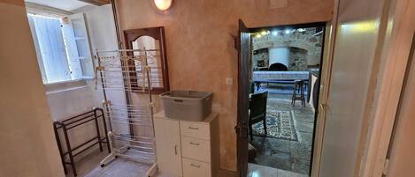 A narrow hallway with a metal drying rack, a small cabinet, and a door leading to a dining area with a stone fireplace.