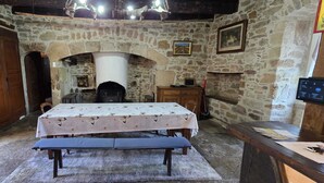 A rustic stone-walled room with a wooden table set for two, a bench, and a fireplace. - Loca saiso/vac/Séjour : 120 m² in an authentic, restored farmhouse (Goutrens)