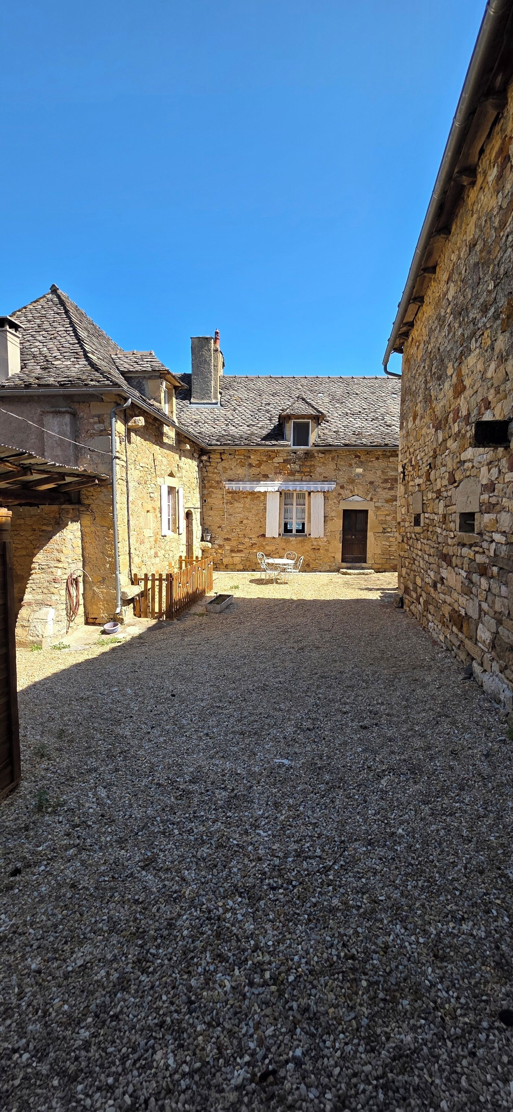 A courtyard with stone buildings, a gravel ground, and a wooden fence.