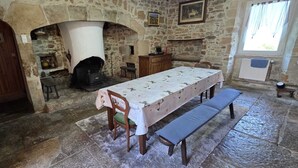 A stone-floored dining area with a table set for two, benches, and a fireplace. - Loca saiso/vac/Séjour : 120 m² in an authentic, restored farmhouse (Goutrens)