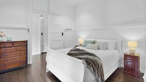 Une chambre à coucher comprenant un lit, une commode, une table de chevet et une porte donnant sur une autre pièce.