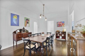 A dining area with a wooden table and chairs, a chandelier, and artwork on the walls. - Rambling Roses: Timeless Retreat in Witta for 8 (Witta)