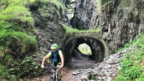 A mountain biker riding through a rocky path with a tunnel in the background. - Olive Tree House- Vacation Rentals (Riva del Garda)