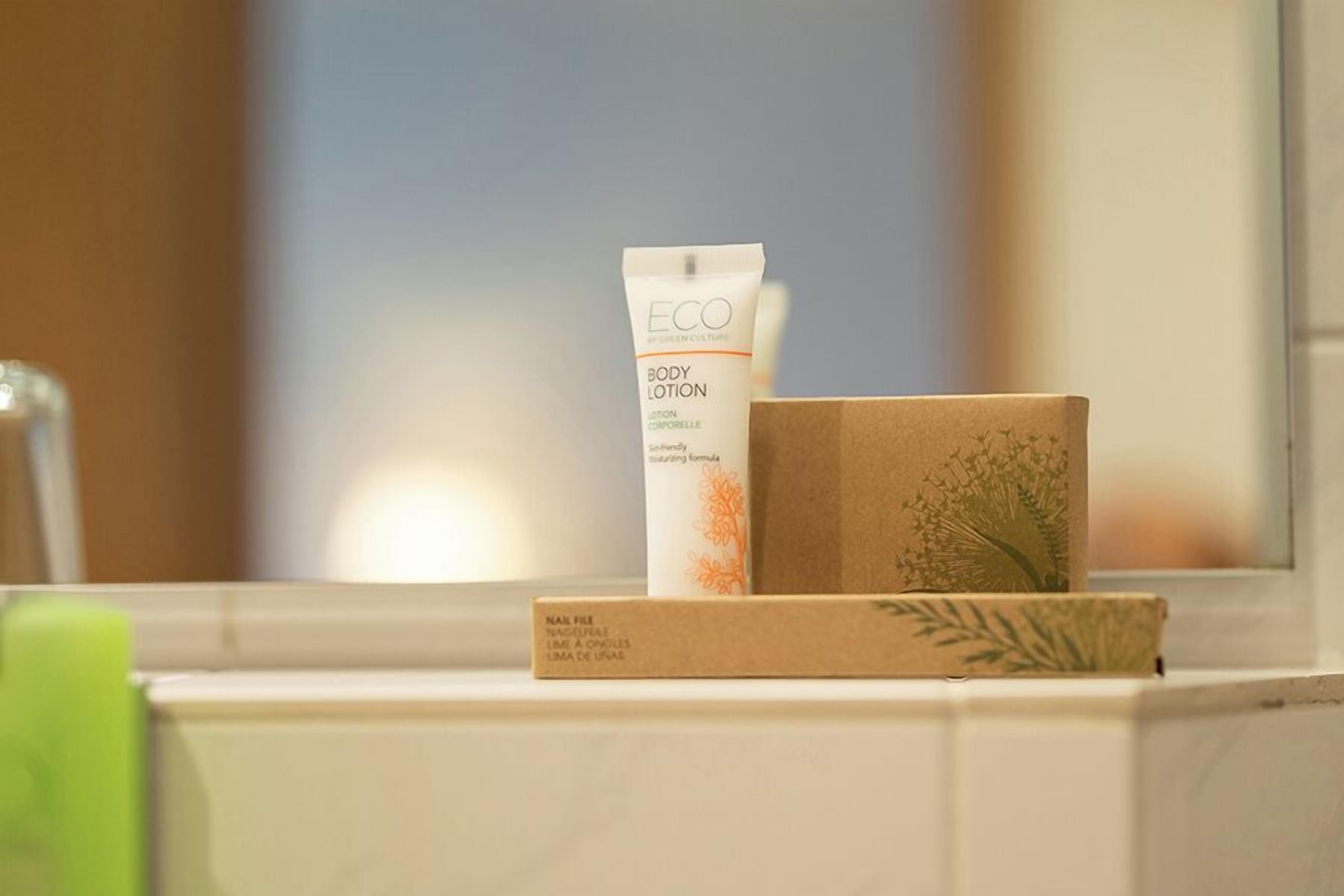 A bathroom with a white bathtub, a green bottle, and a white tube of body lotion on the edge.