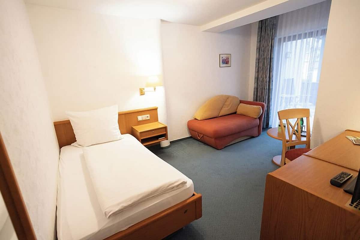 Una habitación de hotel con una cama, un escritorio, una silla, un pequeño sofá y una mesita de noche con lámpara.