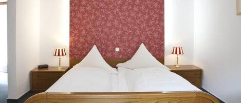 Un lit bien fait, avec deux oreillers, deux lampes de chevet et une tête de lit à motifs floraux.