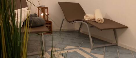 A room with a bed, a small table with a candle, a chair with towels, and a painting on the wall.