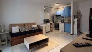 Un espacio habitable pequeño con sofá, una pequeña cocina y zona de comedor.