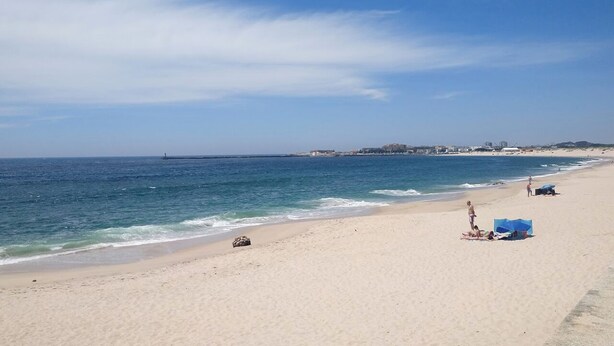 Una playa con cielo despejado, mar tranquilo y un muelle distante.