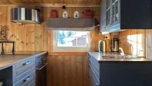 A compact kitchen with wooden paneling, a window with a view of trees, a stainless steel kettle, and a sink. - Lovely home in Sjusjøen with WiFi (Sjusjøen)