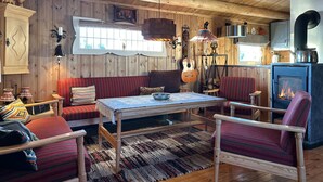 A cozy cabin interior with a wooden floor, a dining table, a sofa, and a chair. There is a fireplace and a guitar hanging on the wall. - Lovely home in Sjusjøen with WiFi (Sjusjøen)