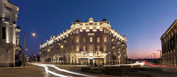 A grand, illuminated hotel with classical architecture, featuring multiple balconies and a prominent entrance.