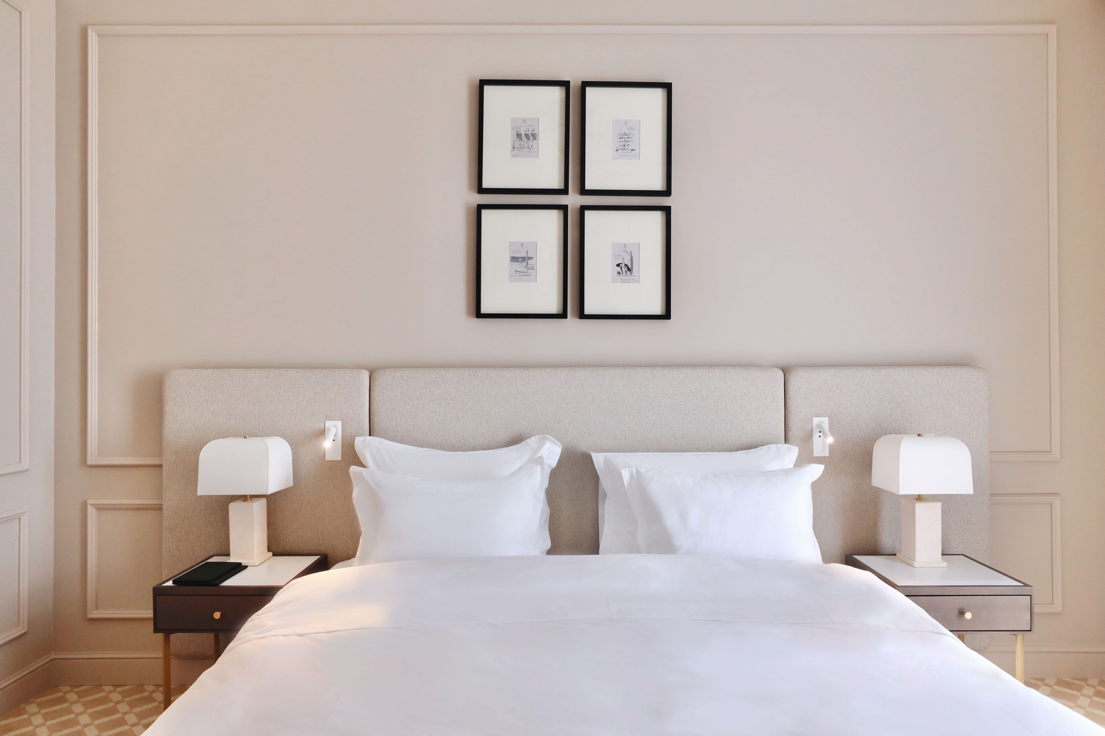Quarto de hotel com uma cama grande, duas mesas de cabeceira com luminárias e uma parede com quatro quadros emoldurados.