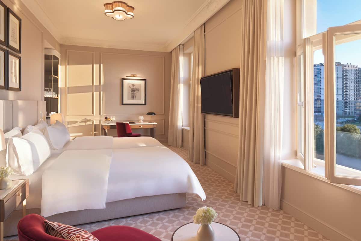 A hotel room with a large bed, a desk, a chair, a TV, and a window with a city view.