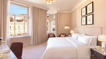 Una habitación de hotel con una cama grande, un escritorio con silla, una ventana con cortinas y cuadros en la pared.