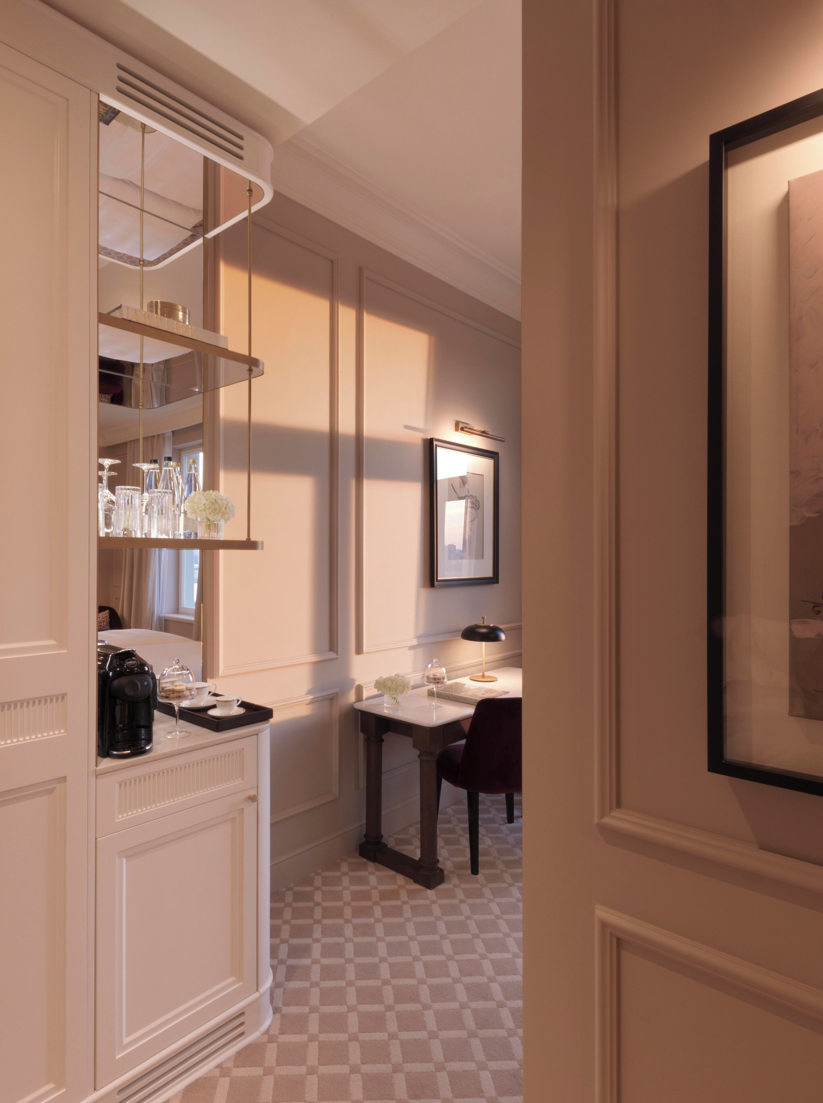 A hotel room with a checkered floor, a dining area with a table and chairs, a coffee machine, and a mirror on the wall.