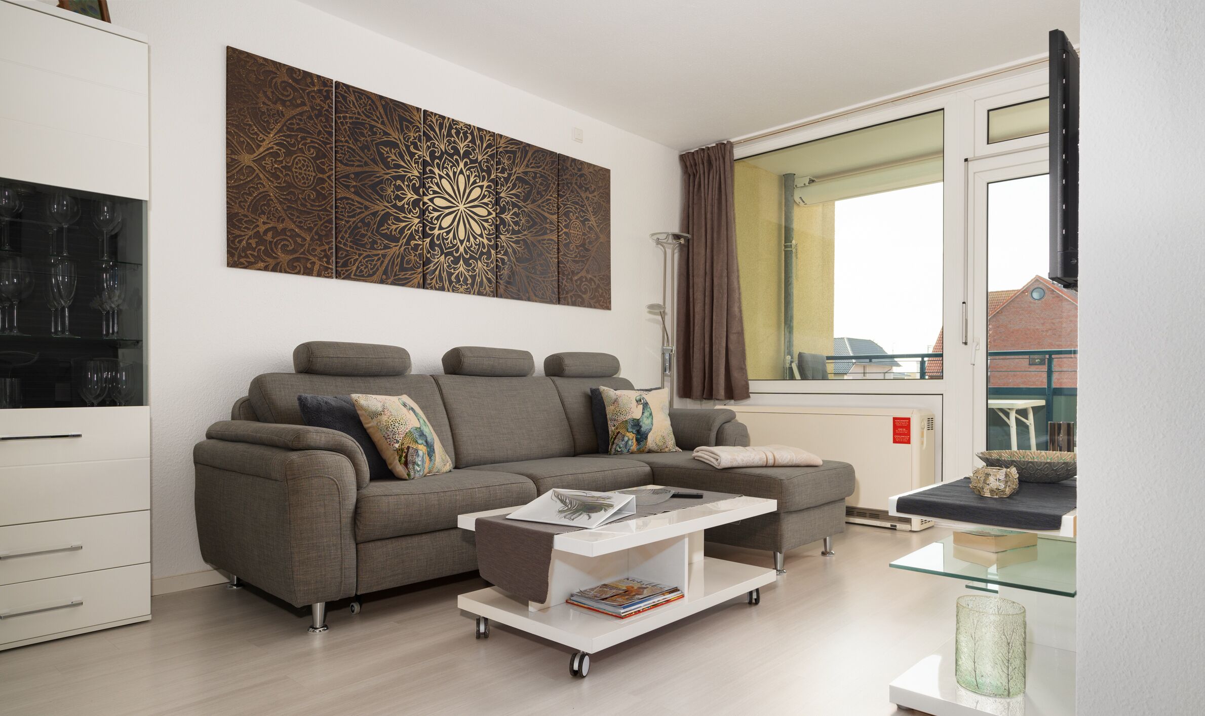 A modern living room with a grey sectional sofa, a glass coffee table, and a large window with curtains.