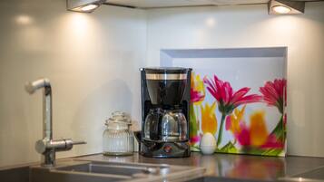 A kitchen with a coffee maker, a glass jar, and a colorful flower painting on the wall.