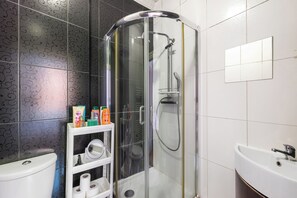 A bathroom with a glass-enclosed shower, a toilet, a sink, and a shelf with toiletries. - Apartment Sleeps 6 With Ensuite Baths (London)