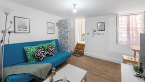 Una sala de estar moderna con un sofá azul, una mesa de centro blanca y una escalera que sube a un piso superior.