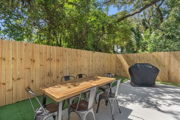 A wooden deck with a table and chairs, surrounded by a wooden fence and trees.
