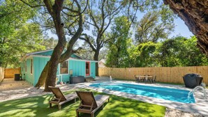 Un patio trasero con piscina, dos sillones de descanso, una terraza de madera y un cerco de madera.