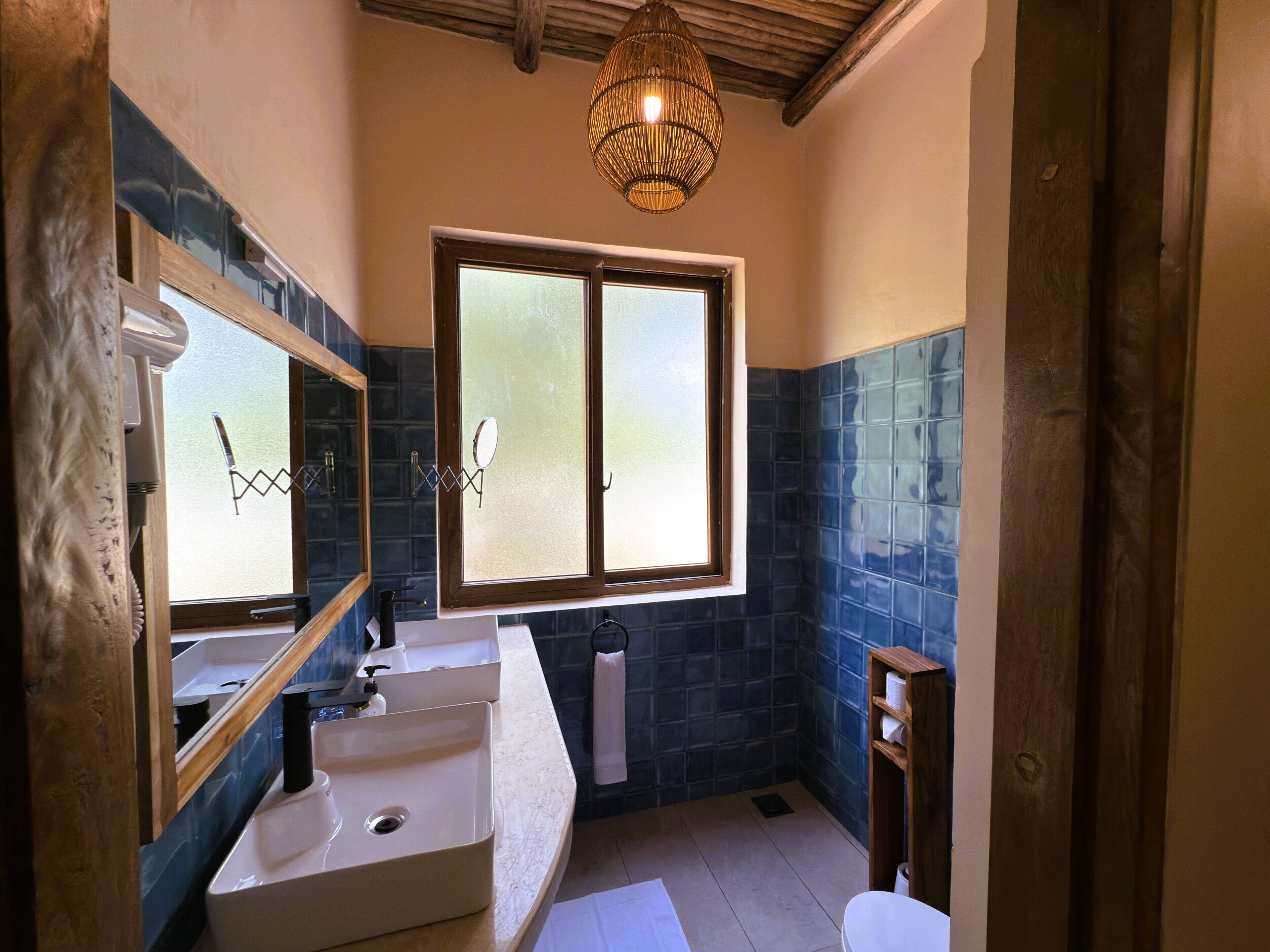 Ein Badezimmer mit zwei Waschbecken, einem großen Spiegel, einem Fenster und einer Pendelleuchte.