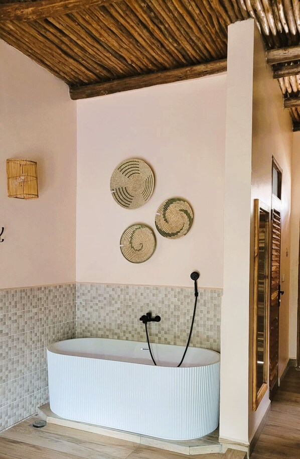 A bathroom with a freestanding bathtub, mosaic tile backsplash, and a wooden ceiling.